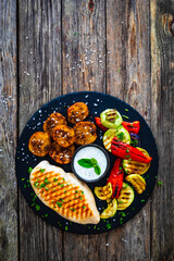 Grilled chicken breast, baked potatoes and barbecued  vegetables on wooden table
