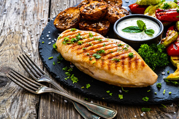 Grilled chicken breast, baked potatoes and barbecued  vegetables on wooden table
