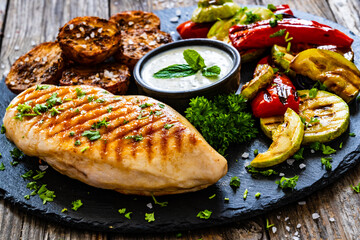 Grilled chicken breast, baked potatoes and barbecued  vegetables on wooden table
