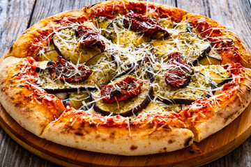 Pizza with eggplant, sun dried tomatoes and parmesan cheese on wooden table
