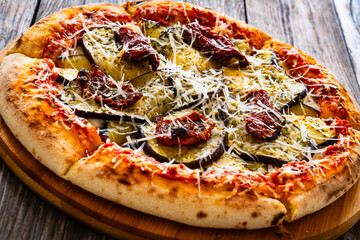 Pizza with eggplant, sun dried tomatoes and parmesan cheese on wooden table
