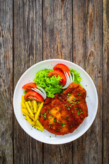 Breaded seared pork chop with fresh vegetable salad and French fries on wooden table 