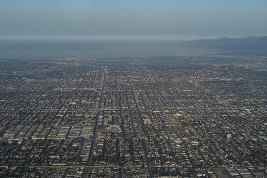 An aerial view over Los Angeles, looking towards the Pacific Ocean. The cityscape shows a massive grid of low-rise, mostly one- and two-story buildings, all the way to the beach.