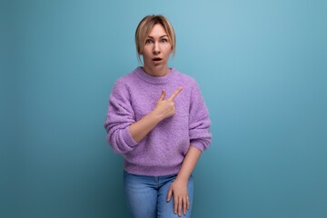 portrait of a shocked surprised blond young woman in a casual look shows her hand to the side on a bright background with copy space