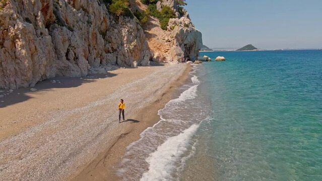 Aerial drone footage relaxed woman traveler walking by Empty Wild secret beach in bay close to Antalya. pebble beach with hi cliffs and clear turquoise waters in Mediterranean Sea. nature of Turkey.