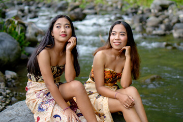 Two young beautiful Asian women sitting on a rock in a river.