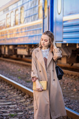 A pretty young woman in a coat and blonde hair stands on the platform of the railway station