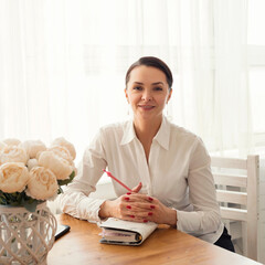 Portrait of a smiling businesswoman sitting at a table with a notebook and a pen
