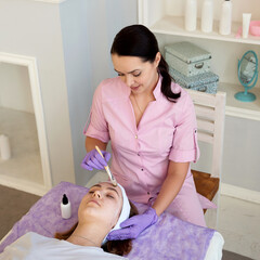beautiful young woman getting facial treatment at beauty salon with beautician
