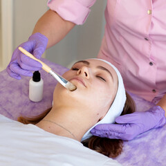 Cosmetologist applying cosmetic mask on the face of a young woman