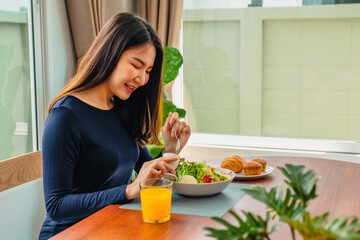 Healthy asian woman eating healthy vegetarian salad while relaxing at home happily.