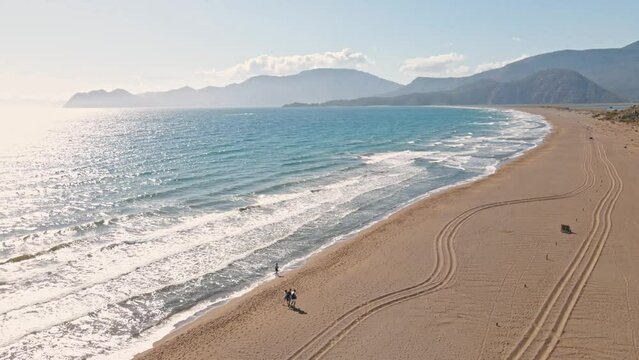 Aerial view flying over tropical white sand beach at sunrise, Iztuzu Turtle Beach, Turkey. people walking along long sand empty beautiful beach at sunny day. summer vacation travel and tourism