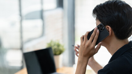 young businessman having document and pencil in hands, speaking on smart phone about important things at desk