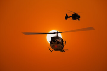 Naklejka na ściany i meble Silhouette helicopter military army practice training flying survey area with orange sun sky background.