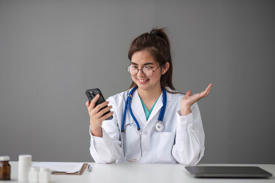 Asian female doctor work at hospital office desk giving patient convenience online service advice, smiling write a prescription order medical with smartphone, health care, preventing disease concept.