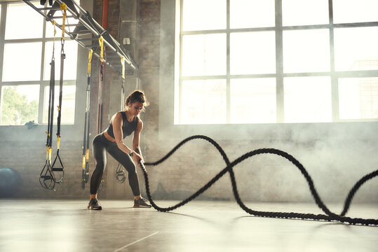 Strong and beautiful. Young athletic woman with perfect body doing crossfit exercises with a rope in the gym.