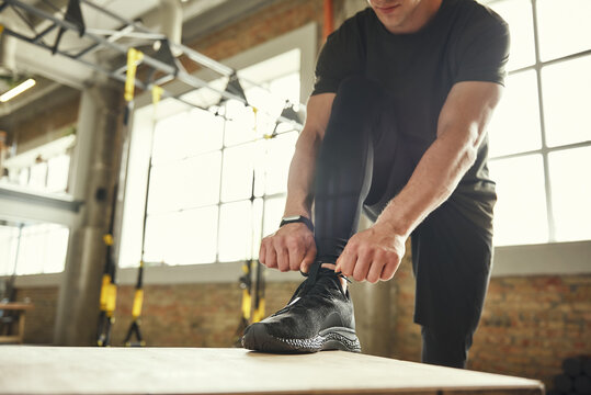 Preparing for workout. Cropped photo of a man in sports clothing tying his shoelaces while exercising in gym.