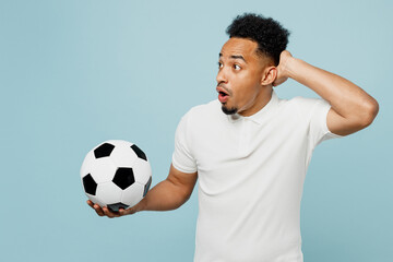 Side view shocked young man fan wears basic t-shirt cheer up support football sport team scratch head look aside hold soccer ball watch tv live stream isolated on plain blue color background studio.