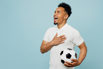 Side view young man fan wearing basic t-shirt sing national country anthem cheer up support football sport team hold in hand soccer ball watch tv live stream isolated on plain blue color background. - obrazy, fototapety, plakaty