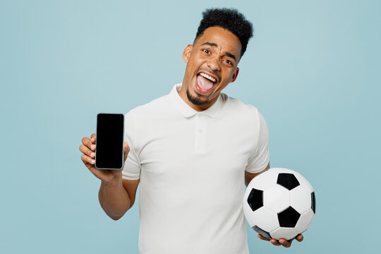 Young man fan wear basic t-shirt use blank screen mobile cell phone cheer up support football sport team hold in hand soccer ball watch tv live stream isolated on plain pastel blue color background