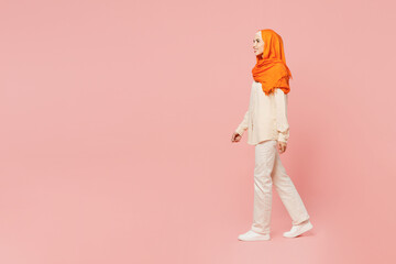 Full body side profile view smiling young arabian asian muslim woman wear orange abaya hijab walk...
