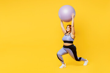 Full body young chubby plus size big fat fit woman wear blue top warm up training hold in hands fit ball above head do squats isolated on plain yellow background studio home gym Workout sport concept