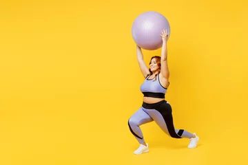 Deurstickers Fitness Full body young chubby plus size big fat fit woman wear blue top warm up training hold in hands fit ball above head do squats isolated on plain yellow background studio home gym Workout sport concept