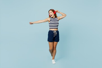 Full body young woman she wear striped tank shirt casual clothes headphones listen to music raise up hand dance isolated on plain pastel light blue cyan background studio portrait. Lifestyle concept.