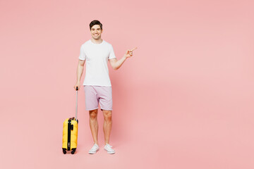 Traveler fun man wear summer casual clothes hold suitcase point aside isolated on plain pink background studio. Tourist travel abroad in free spare time rest getaway. Air flight trip journey concept.