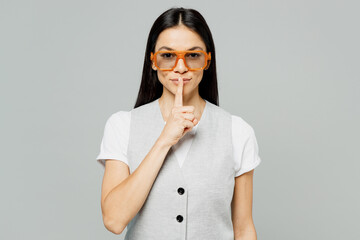 Young secret latin woman she wear white t-shirt gray vest glasses say hush be quiet with finger on...