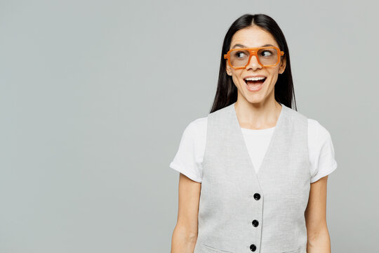 Young surprised shocked impressed astonished happy latin woman she wear white t-shirt gray vest glasses look aside on area mock up isolated on plain grey background studio portrait. Lifestyle concept.