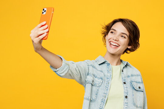 Young woman she wear green t-shirt denim shirt casual clothes doing selfie shot on mobile cell phone post photo on social network isolated on plain yellow background studio portrait Lifestyle concept