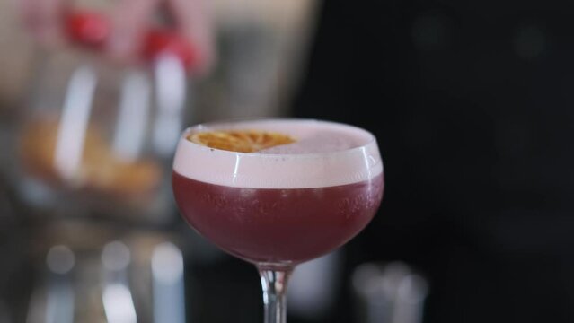 A bartender in an expensive edith hotel pours a prepared pink cocktail from a shaker into a glass and decorates with a slice of lemon