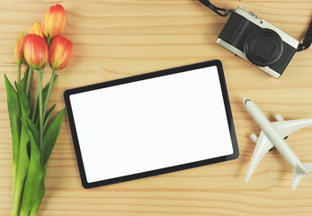 flat lay of digital tablet with blank white screen, tulip flowers, airplane model and  digital camera isolated on wooden table background.