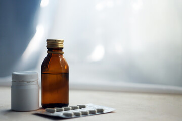 Bottle with medicine and pills in the room on the background of white sunlit curtain. Free space for inscription. The concept of hope for a speedy recovery, taking care of the health of loved ones.