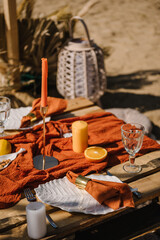 Lunch, romantic orange colors. Picnic with blanket, napkin, pillows, candles, wooden decor, dry flowers. Bachelorette party on beach. Boho style design picnic. Decorations for celebration birthday.