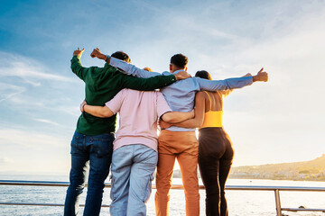 Diverse Friends Embracing at Sunset - Four friends of diverse ethnicities, seen from behind, embrace and face the setting sun.