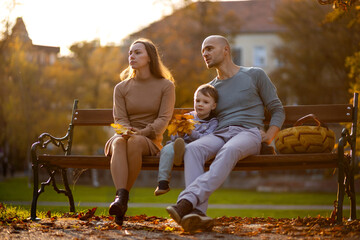 Woman is sad on a bench next to her husband and son on an autumn day in the park