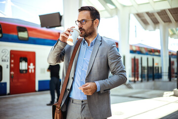 Businessman holding a disposable coffee cup at the train station platform. A man in a train station...