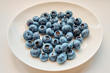 Fresh blueberries lie on a white plate on a dark background. Berries, healthy food. Selective focus. View from above.