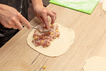 A woman prepares pies from dough and minced meat on the table