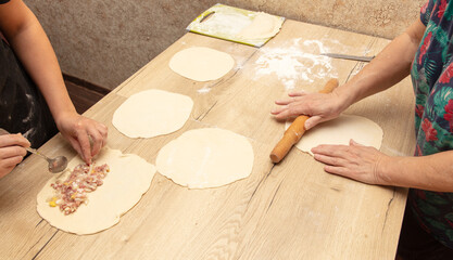 Women prepare pies from dough and minced meat on the table