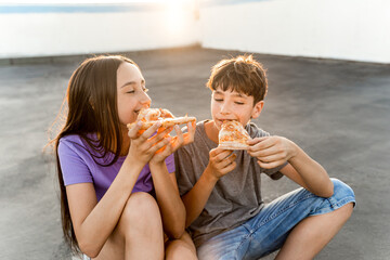Two Caucasian teenagers eating pizza at sunset