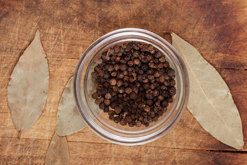 Peppercorns in glass bowl on wooden background with bay leaves. Seasoning mix, top view. 