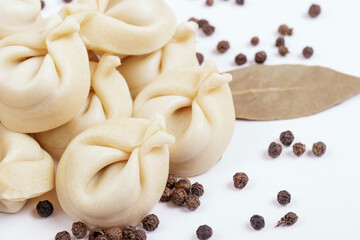 Uncooked dumplings with peppercorns and bay leaves on white background. Dumplings closeup.