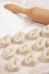 Dumplings on a wooden board, flour and rolling pin on the table. Homemade dumplings closeup.