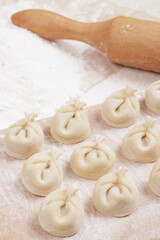 Dumplings on a wooden board, flour and rolling pin on the table. Homemade dumplings closeup.