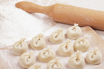 Dumplings on a wooden board, flour and rolling pin on the table. Homemade dumplings closeup.