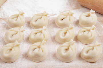 Fototapeta na wymiar Dumplings on a wooden board, flour and rolling pin on the table. Homemade dumplings closeup.