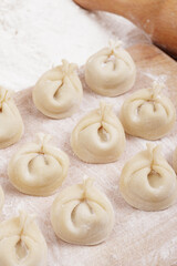 Dumplings on a wooden board, flour and rolling pin on the table. Homemade dumplings closeup.